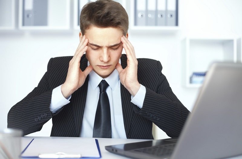 Tired young businessman with problems and stress at his workplace in bright office