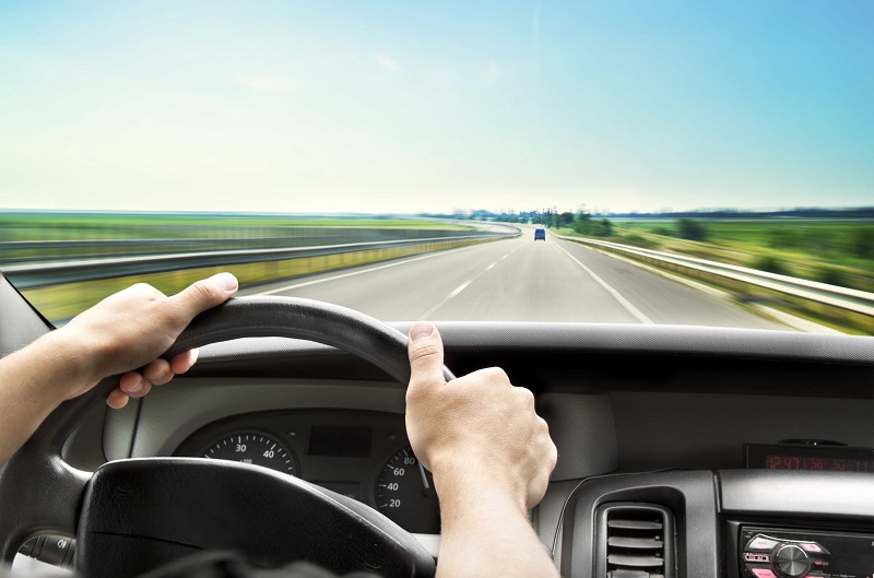 Man's hands of a driver on steering wheel of a minivan car on asphalt road