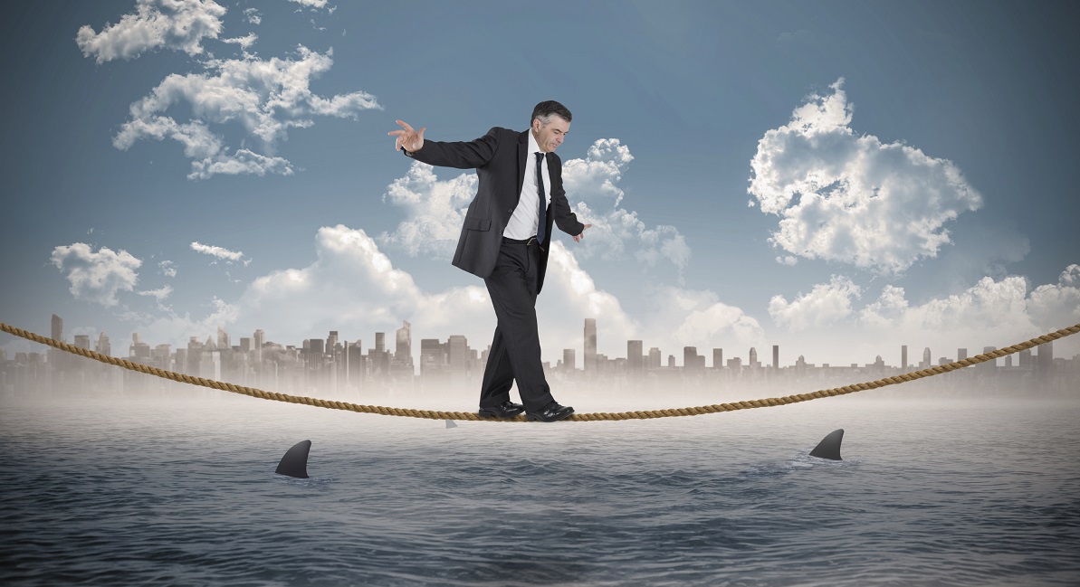 Mature businessman doing a balancing act against cityscape on horizon over shark infested sea