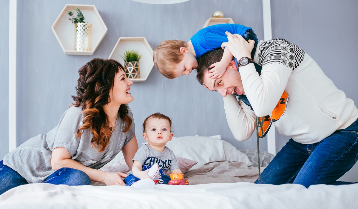 The mother ,father and sons sitting on the bed
