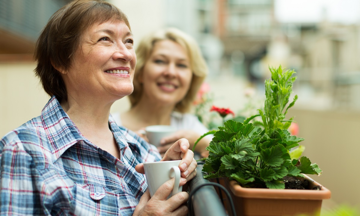 Smiling senior women staying on balcony with cup of coffee in hands