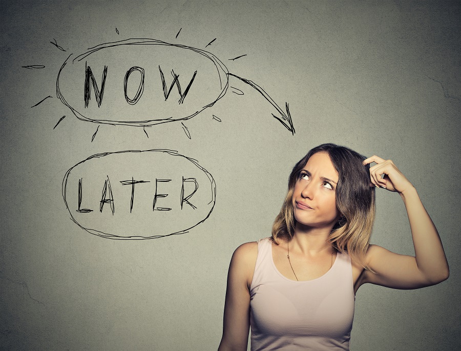 Now or later. Woman thinking scratching head looking up isolated on grey wall background. Human face expression