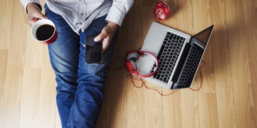 Soft photo of man felling comfort use smartphone on the wooden floor with cup of coffee, headphone, computer laptop and clock, Top view point of copyspace relax time.