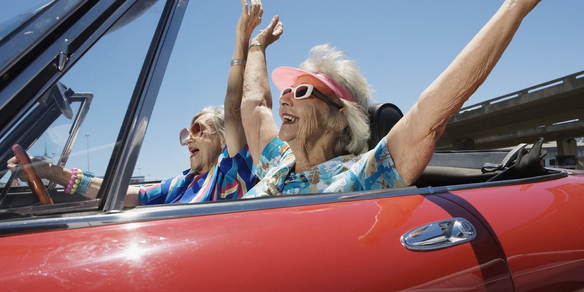 Two senior women in convertible car, arms outstretched, side view