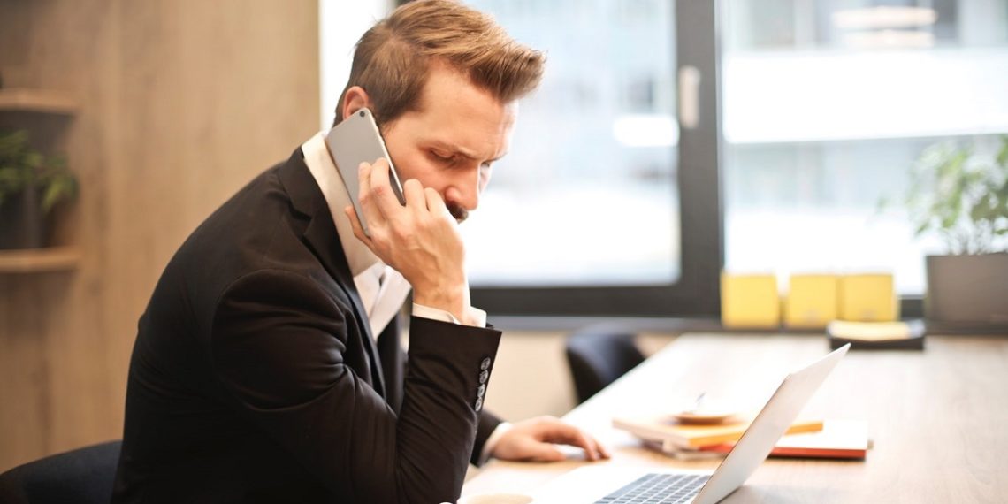 man-having-a-phone-call-in-front-of-a-laptop-insurancedaily