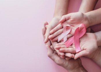 hands holding pink ribbons on pink background, Breast cancer awareness and October Pink day