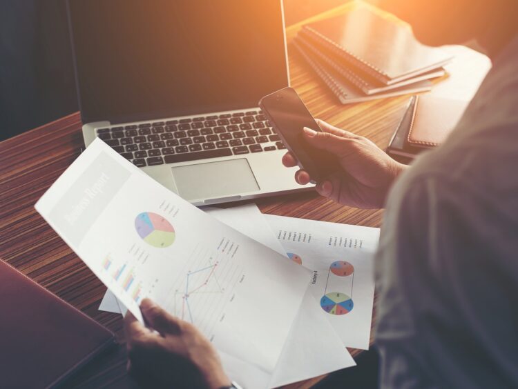 Businessman hands using cell phone with financial report graph at office desk.