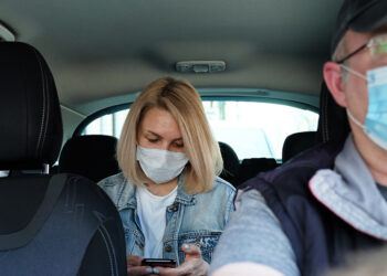 Caucasian woman in taxi wearing face mask for protection from pollution and viruses such as Coronavirus. Using smartphone