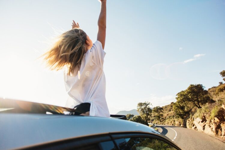woman-car-road-trip-waving-out-window-smiling