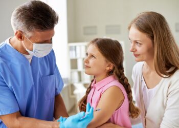 Smiling girl and her mother looking at doctor while he making an injection in clinics