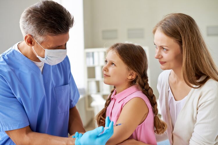 Smiling girl and her mother looking at doctor while he making an injection in clinics