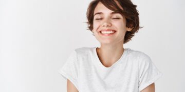 Beautiful caucasian woman dreamy smiling with eyes closed, standing relaxed and happy against white background. Copy space