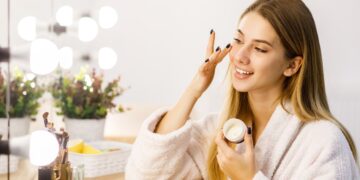 young-beautiful-blonde-girl-cares-face-skin-with-moisturizer-front-mirror