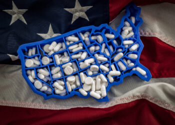 Healthcare, opioid epidemic and drug abuse concept with the map of USA filled with oxycodone and hydrocodone pharmaceutical pills on the American flag