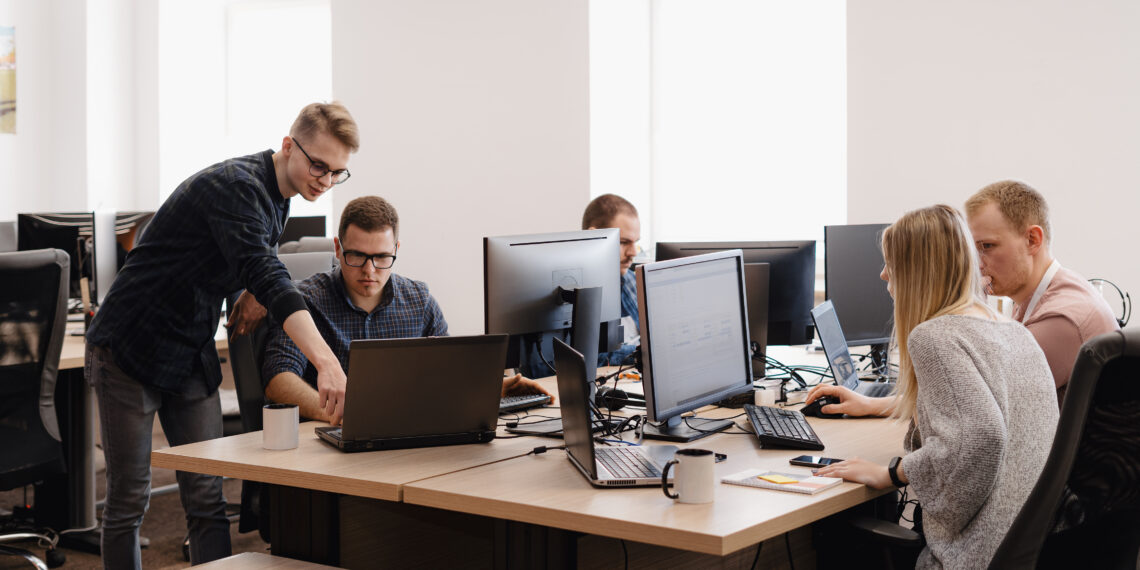 Full concentration at work. Group of young business people working and communicating while sitting at the office desk together with colleagues sitting in the background