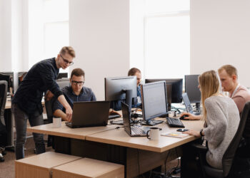 Full concentration at work. Group of young business people working and communicating while sitting at the office desk together with colleagues sitting in the background