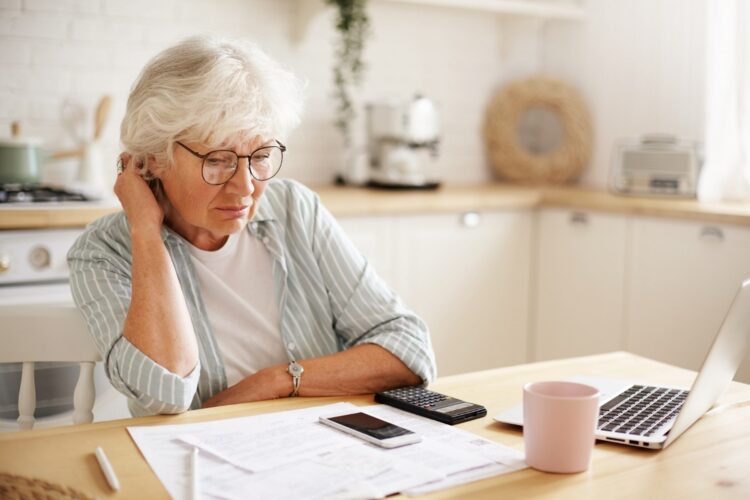 people-age-technology-finances-depressed-unhappy-retired-woman-paying-domestic-bills-online-trying-hard-make-both-ends-meet-sitting-kitchen-table-surrounded-with-papers-using-gadgets
