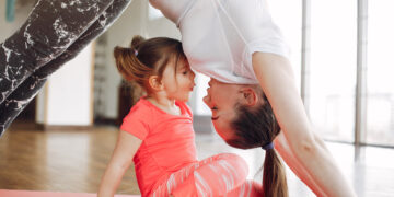 Woman in a sportswear. Mother with little daughter. Family are engaged in gymnastics in a gym
