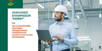 Chief Engineer in the Hard Hat Walks Through Light Modern Factory While Holding Laptop. Successful, Handsome Man in Modern Industrial Environment.