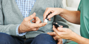Krankenschwester macht eine Blutzuckermessung bei Patient mit Diabetes im Pflegeheim